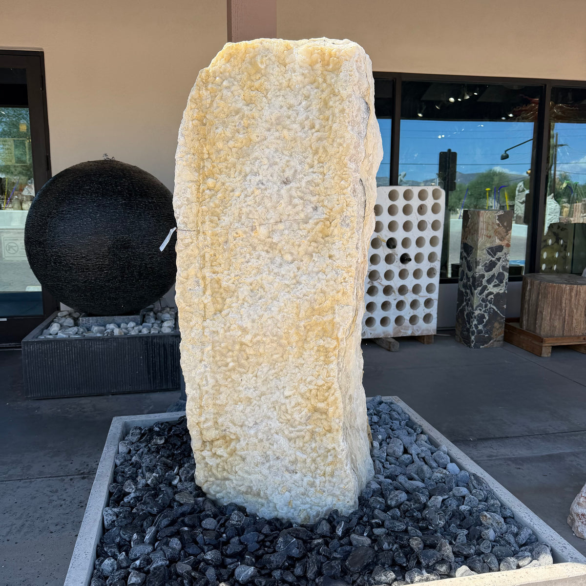 White crystal and gray onyx band fountain, cream travertine pillar set in a black river-rock basin