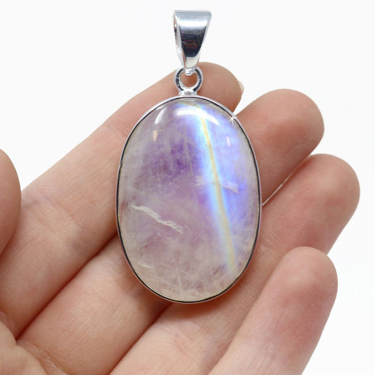 Rainbow moonstone pendant on a silver chain held in a hand against a white background