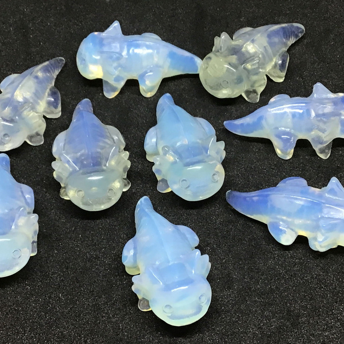 Opalite axolotl carvings with milky blue glow, group of ten shown on black surface