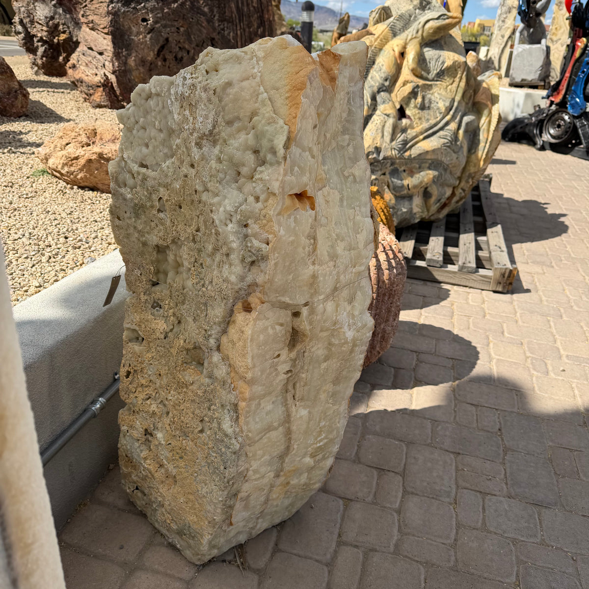 Amber Ice Onyx fountain's crystal-pocked cream face in the outdoor gallery yard beside carved stone sculptures