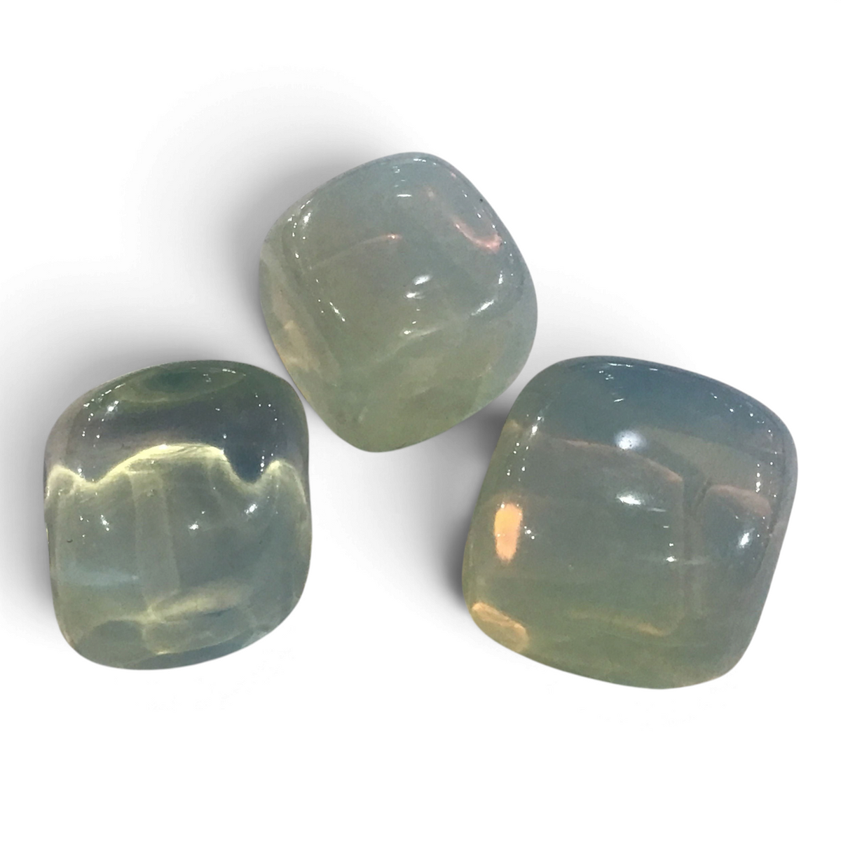 Three tumbled opalite stones with glassy blue-green glow catching warm light