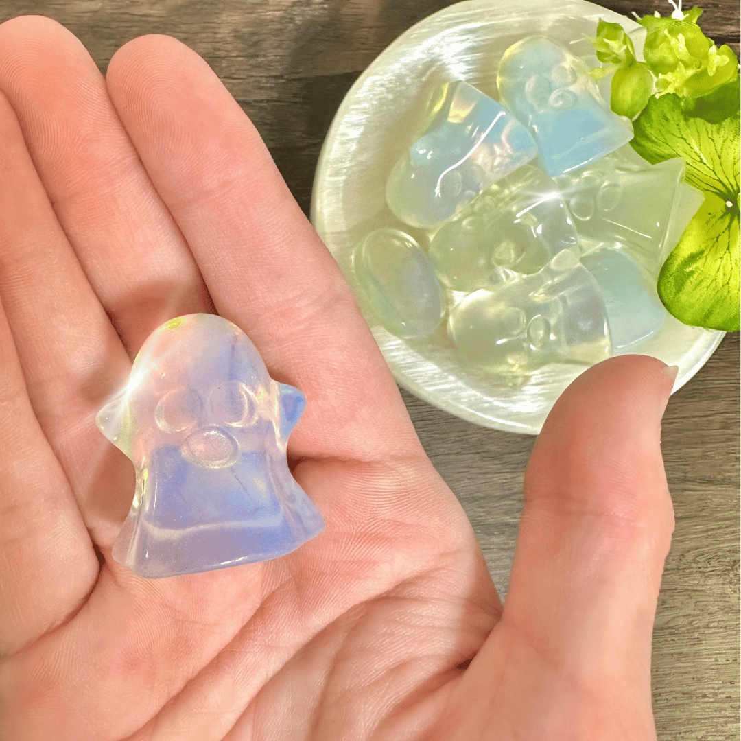 Opalite ghost carving resting in an open palm with a dish of glowing opalite ghosts nearby