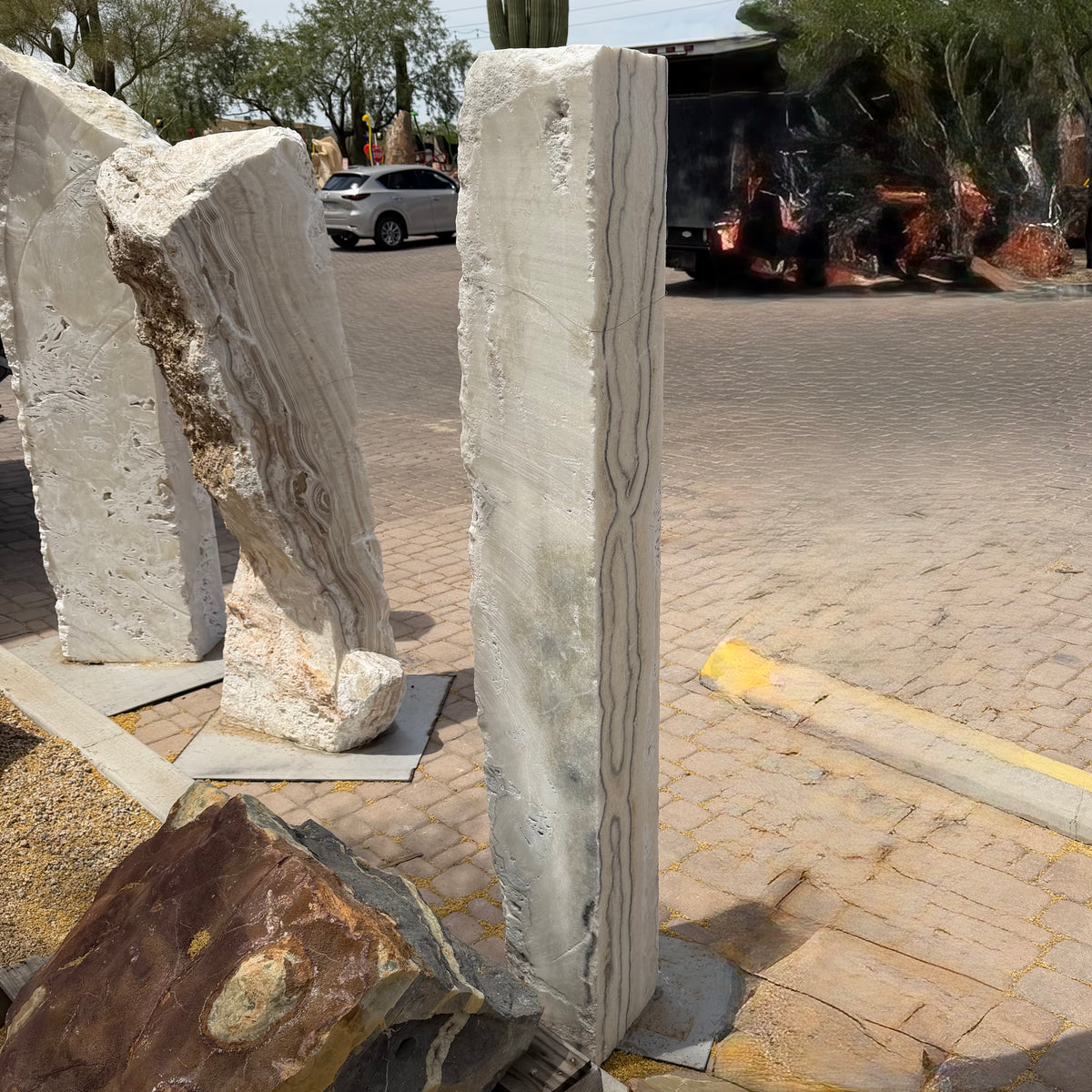 Zebra Fossil Onyx pillar fountain upright on pavers alongside other onyx slab pieces in the outdoor gallery lot
