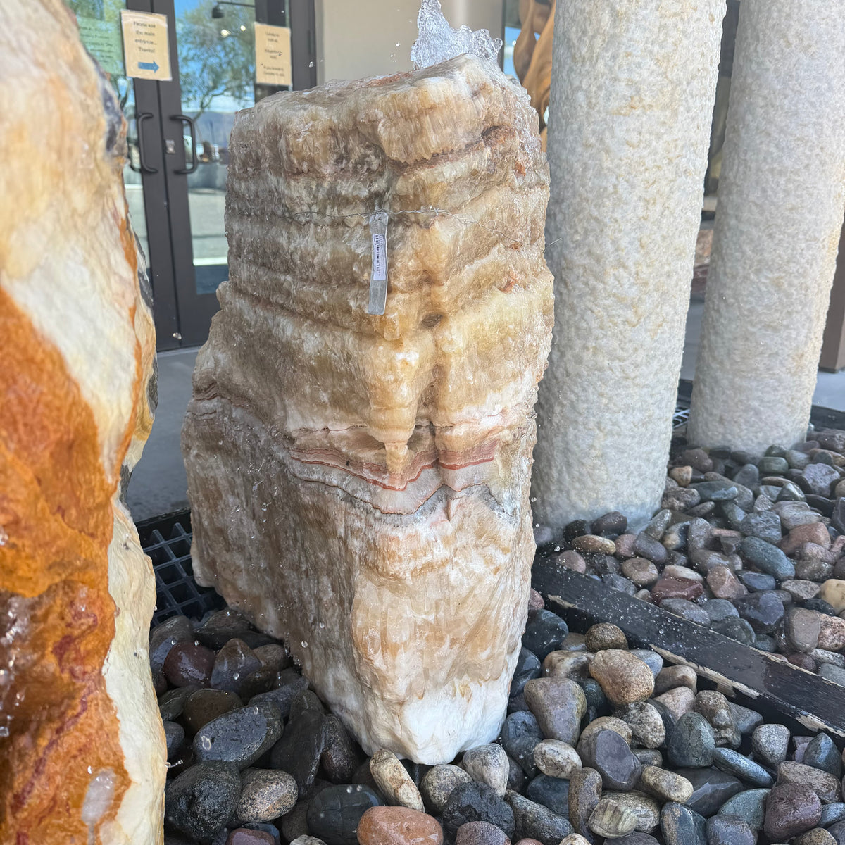 Serpentine onyx layered boulder fountain running on a gravel bed outside the gallery entrance