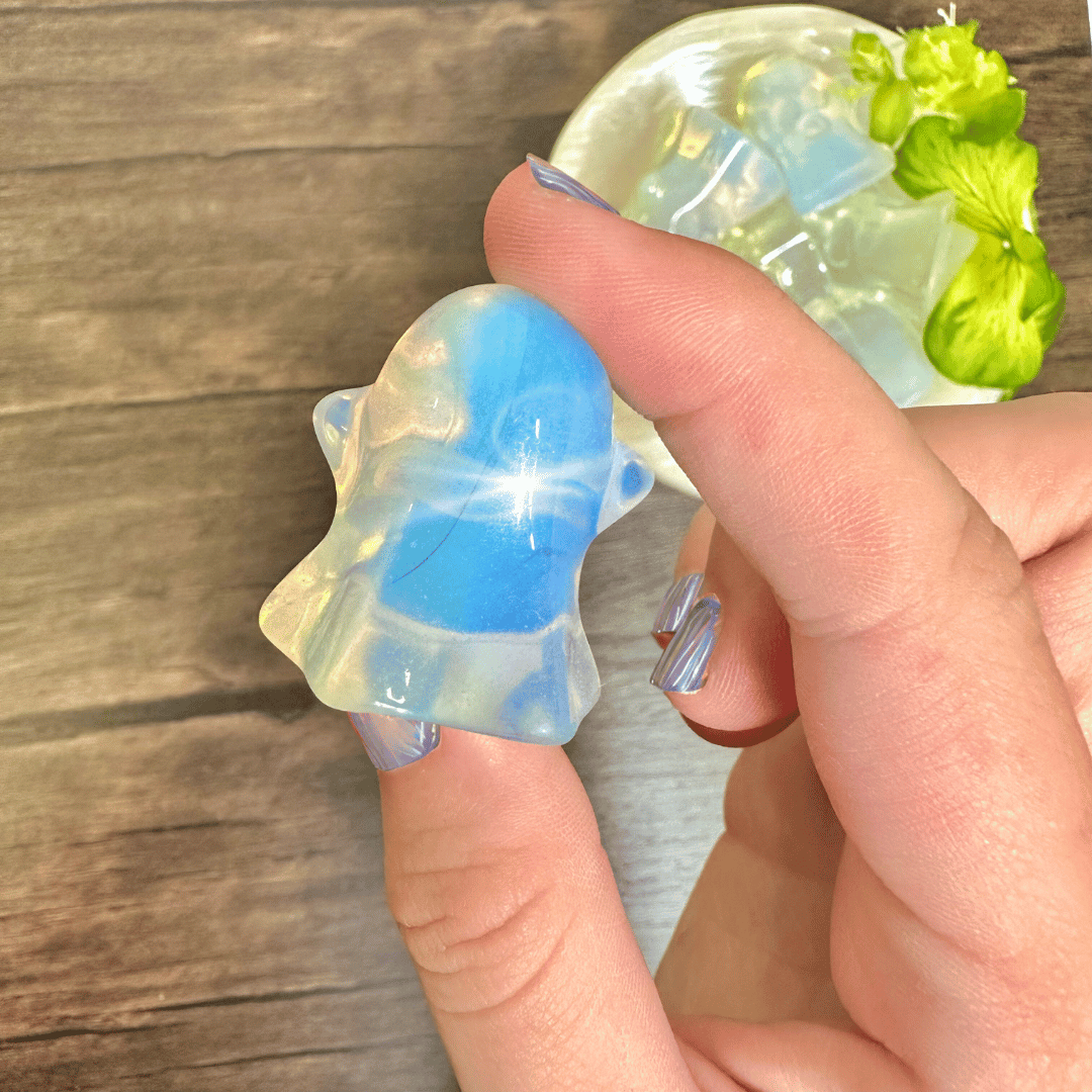 Opalite ghost carving with a vivid blue swirl held up beside a bowl of tumbled opalite ghosts