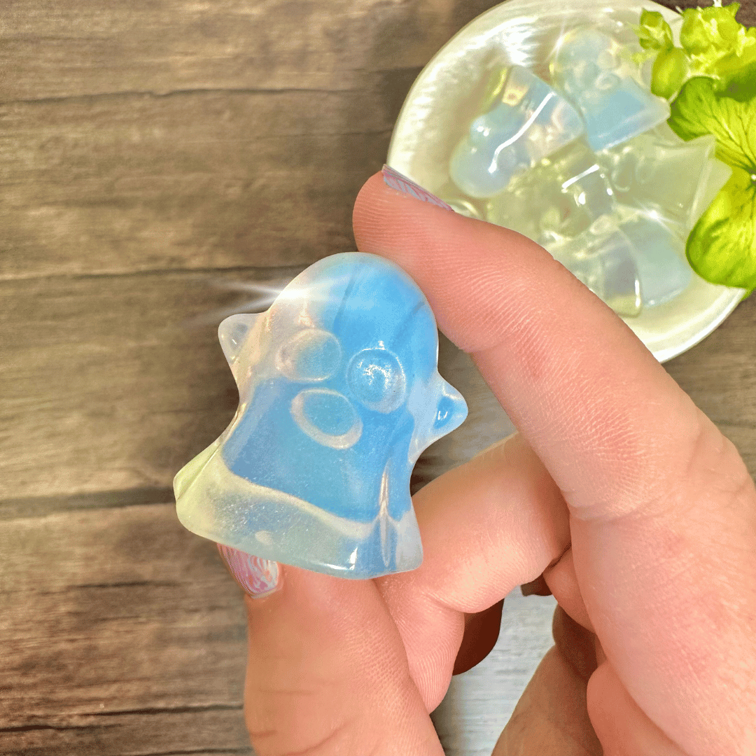 Blue and white opalite ghost carving held between fingertips above a dish of matching ghosts