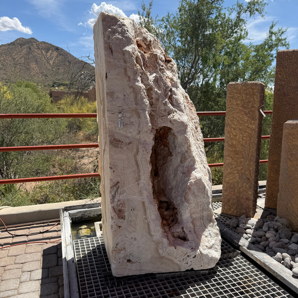 Sunset Fossil Onyx boulder fountain with cavern, rough pale side and deep crevice against a mountain backdrop