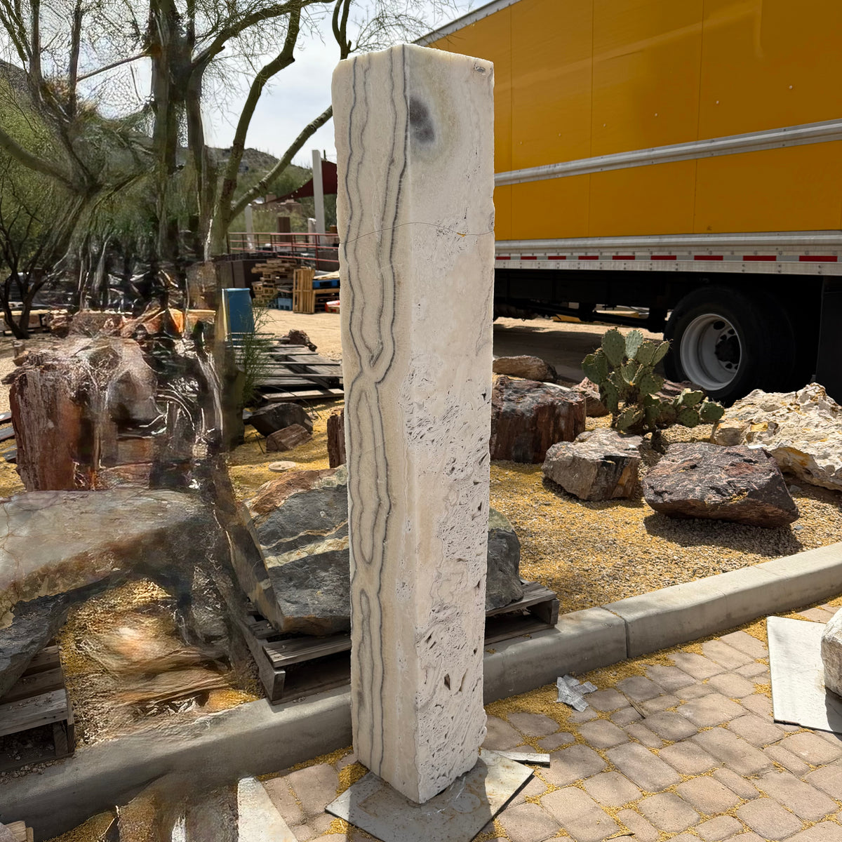 Zebra Fossil Onyx pillar fountain showing gray banded stripes down its cream face, staged near a delivery trailer