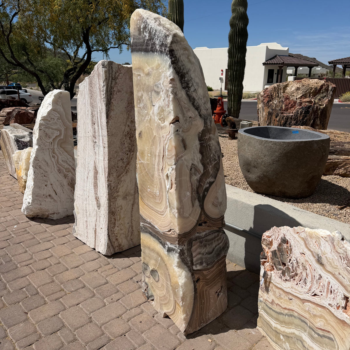 Cosmic Orange Zebra Onyx fountain seen from the side beside other onyx slabs under desert saguaros