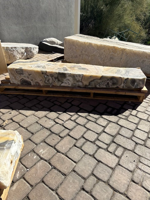 Cosmic onyx fountain pillar resting on a wooden pallet, polished wavy face with gray vugs seen from the side
