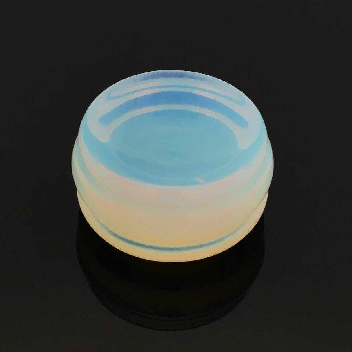 Opalite gemstone sphere stand disc with carved cradle glowing blue and peach on a black reflective surface
