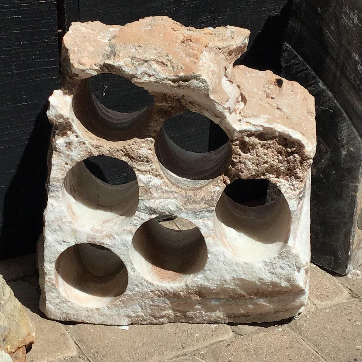 Six-hole rustic onyx wine rack in pale white and blush stone with a rugged unpolished top edge