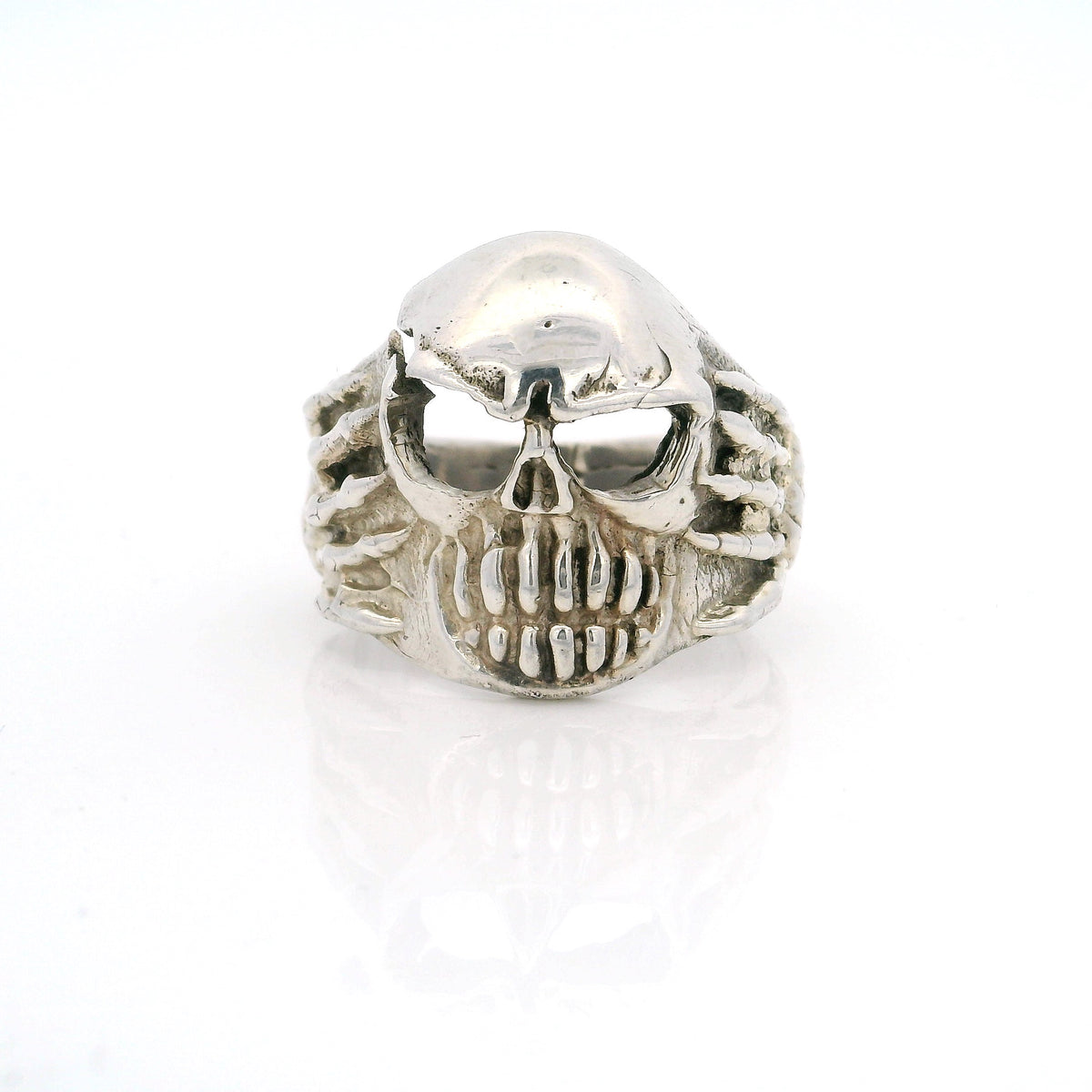 Sterling silver skull ring with bared teeth and skeletal hands at the sides, front view
