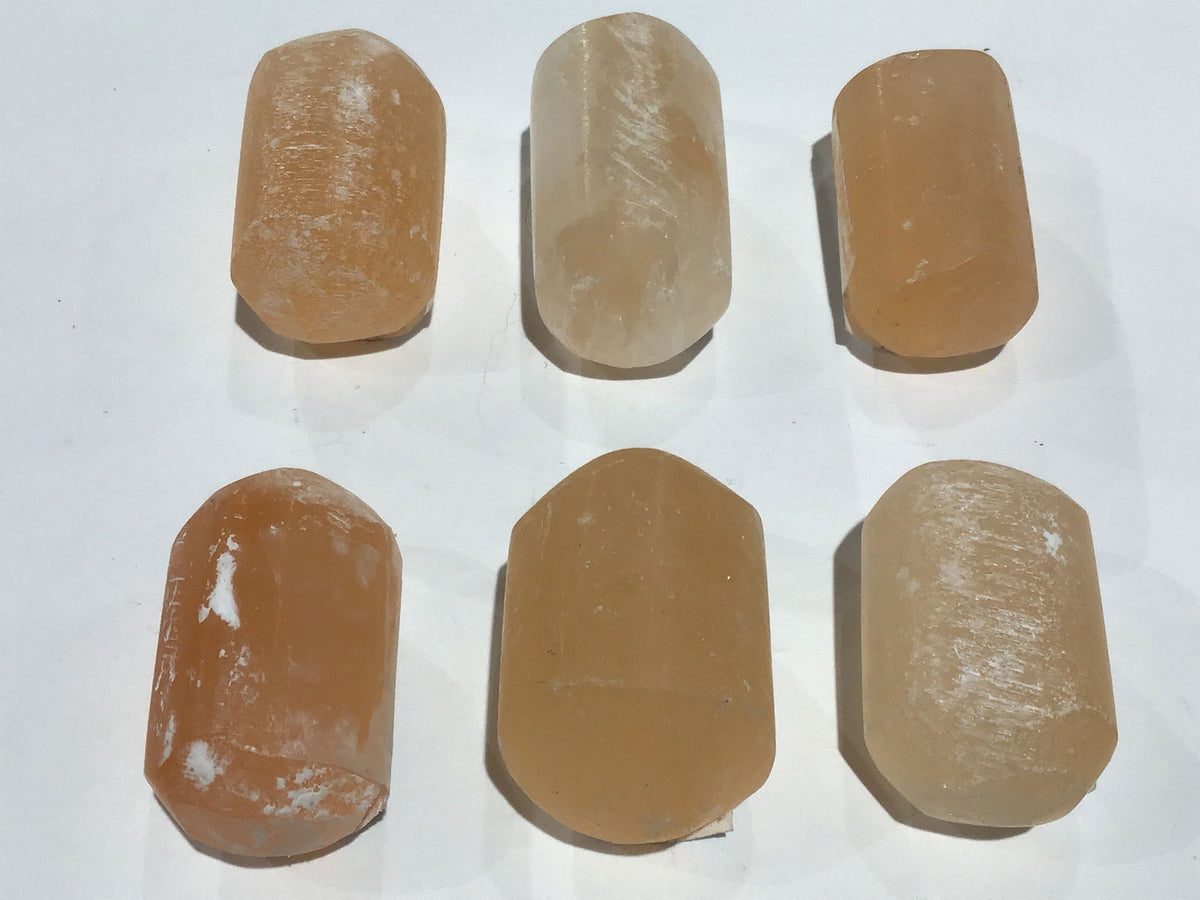 Six tumbled peach selenite stones in warm apricot with satin fibrous sheen, arranged in two rows on white