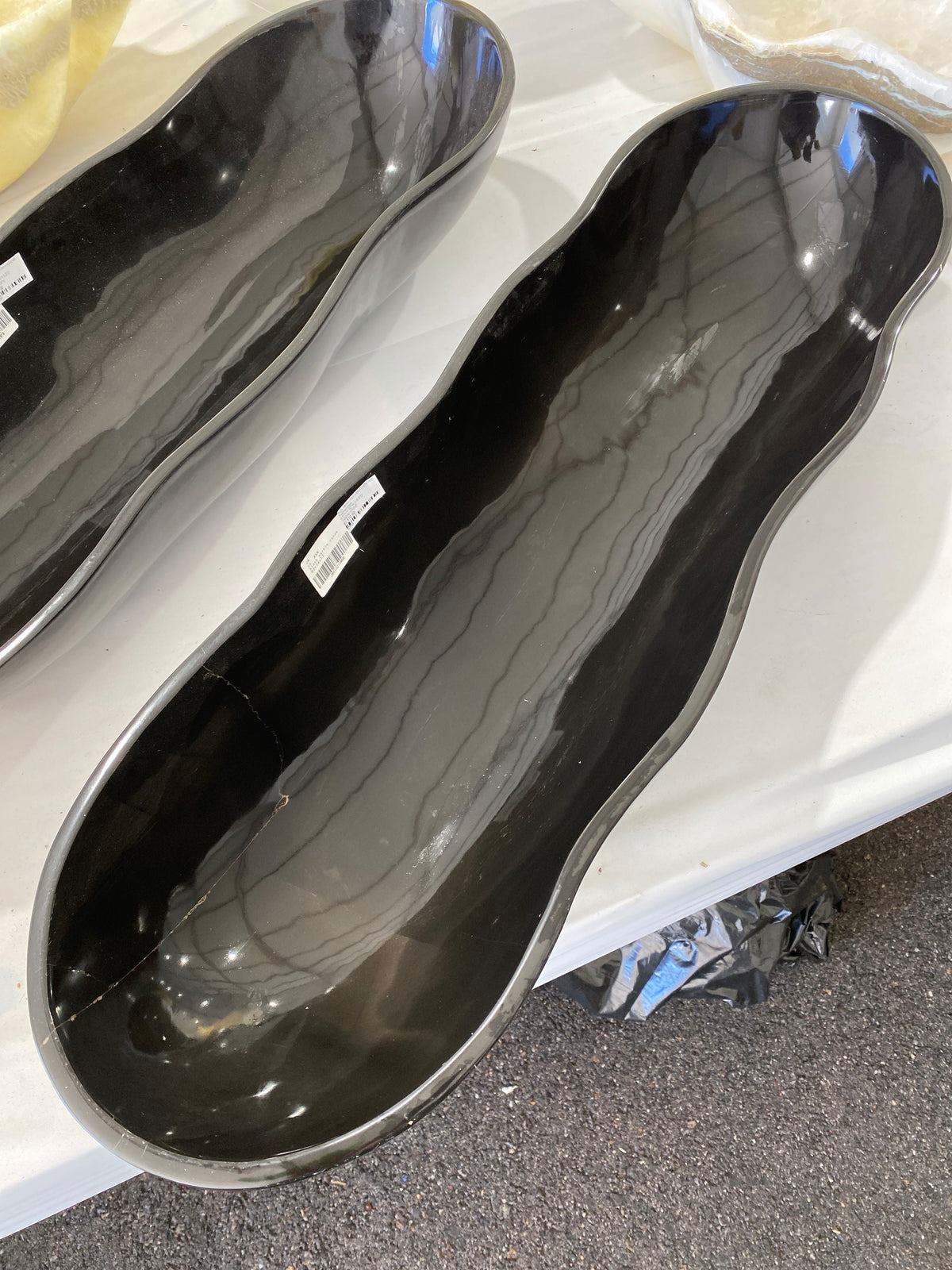 Elongated black marble onyx canoe vessel with wavy polished rim and soft gray banding, beside a second