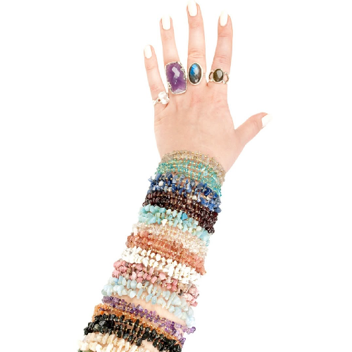 Hand wearing multiple colorful crystal beaded bracelets and gemstone rings on a white background