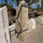Cosmic Orange Zebra Onyx fountain column with tan, cream and charcoal banding standing in an outdoor stone yard