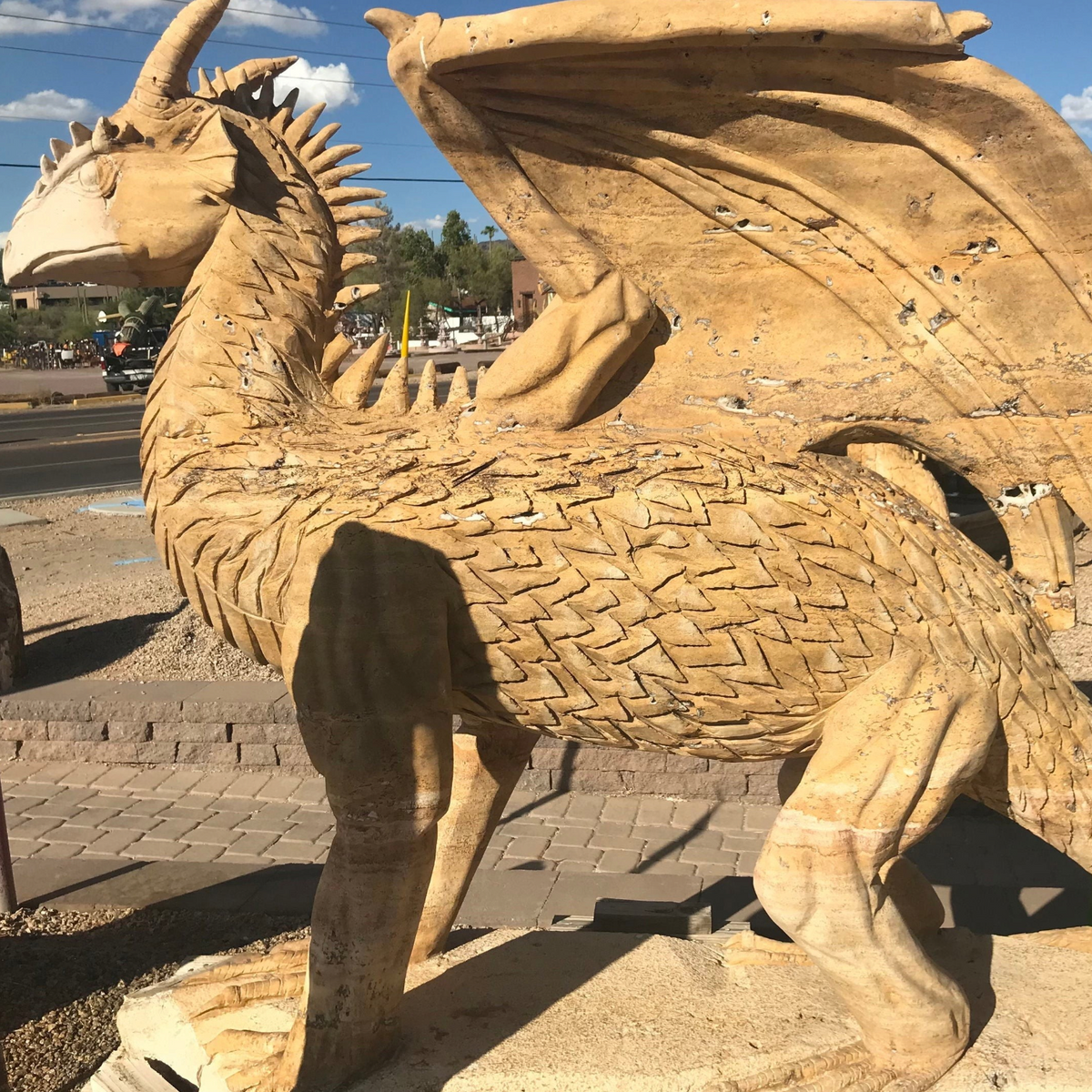 Tan travertine dragon carving in full side profile with raised wing and spiked back, outdoors