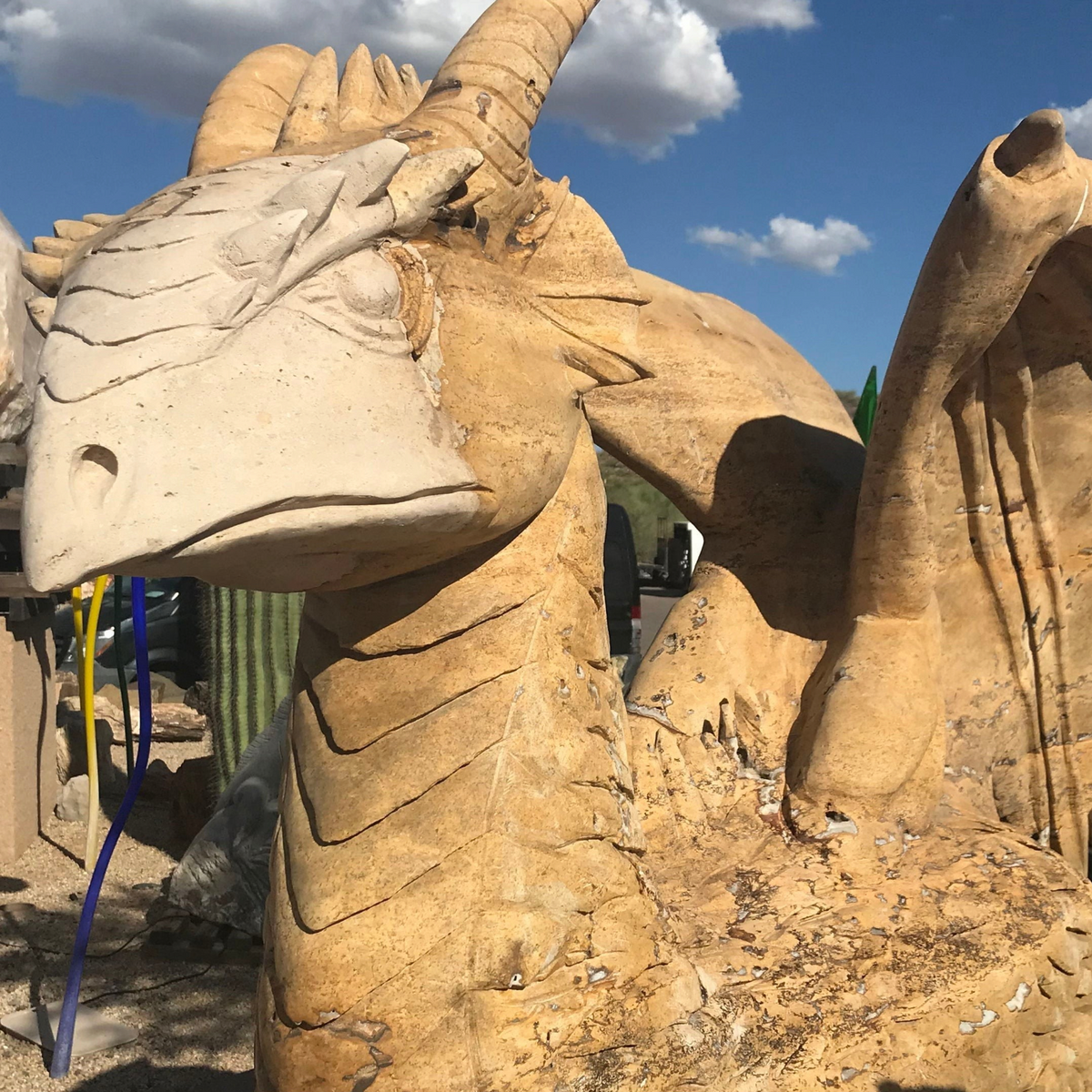 Large tan travertine dragon carving, close-up of horned head with a second dragon beyond, outdoors