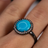 Sleeping Beauty turquoise cabochon ring with CZ halo and dark ruthenium band worn on a finger