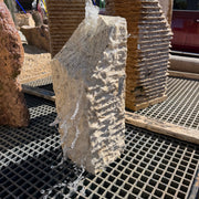 Beige Travertine Chiseled Column with Slanted Top - Short running water down its ridged face in an outdoor fountain yard