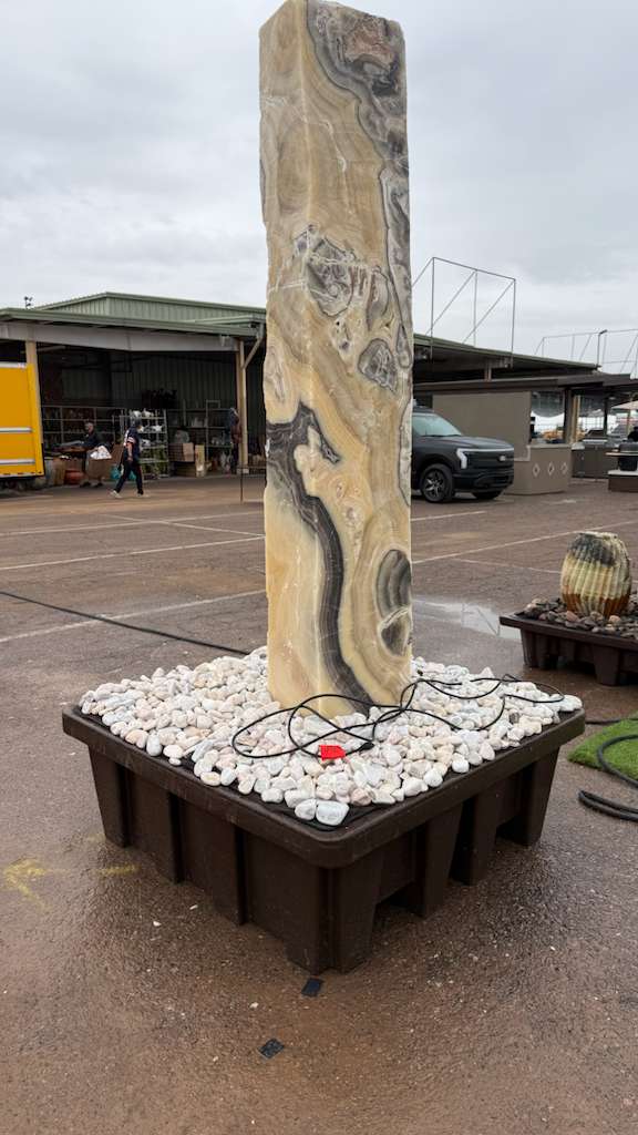 Cosmic onyx pillar fountain standing upright on a basin of white river stones in the gallery yard