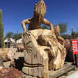 Wooden sculpture of an iguana on a log with cacti and desert landscape in the background
