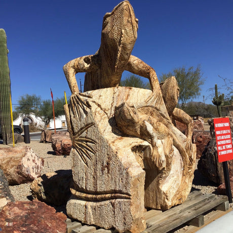 Wooden sculpture of an iguana on a log with cacti and desert landscape in the background