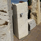 White fossil onyx fountain column standing upright on pavers, porous cream stone face lit by desert sun