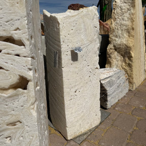 White fossil onyx fountain column standing upright on pavers, porous cream stone face lit by desert sun