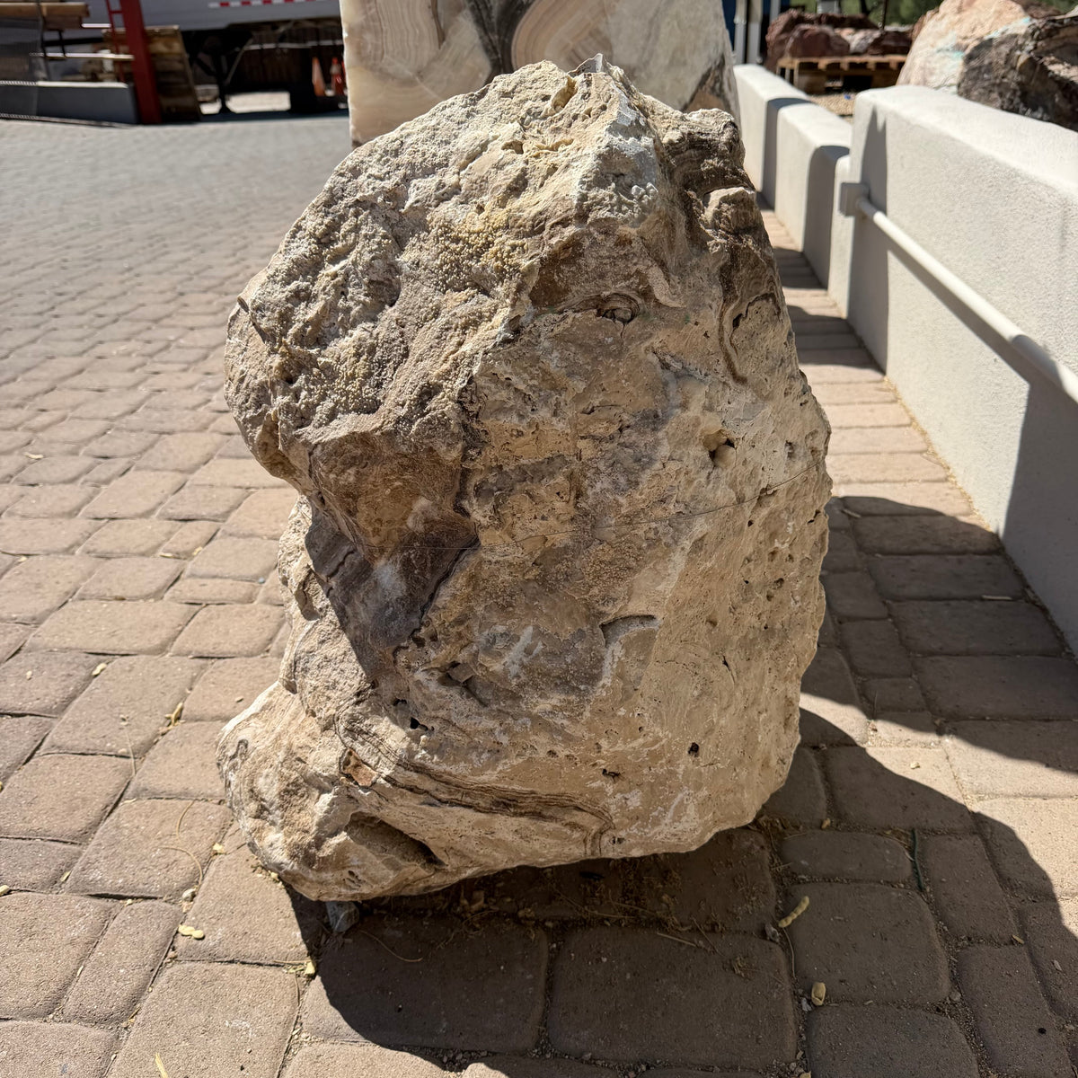 Side view of the chocolate travertine onyx boulder fountain, pitted surface beside a low wall