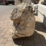 Side view of the chocolate travertine onyx boulder fountain, pitted surface beside a low wall