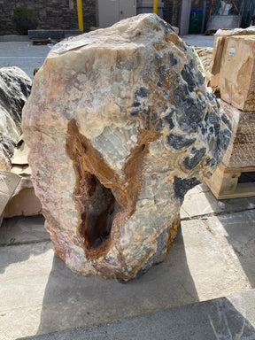 Green Talan Onyx rustic rock fountain with natural stone texture and a hollowed center, displayed outdoors on a concrete s...