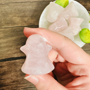Hand holding a rose quartz ghost carving with a carved face, bowl of carvings behind