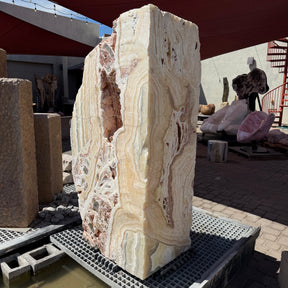 Sunset Fossil Onyx boulder fountain with cavern, cream and peach banding, standing on a gallery yard grate