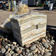 Zebra fossil onyx block fountain with 2 holes set in a river rock basin, horizontal cream and tan banding
