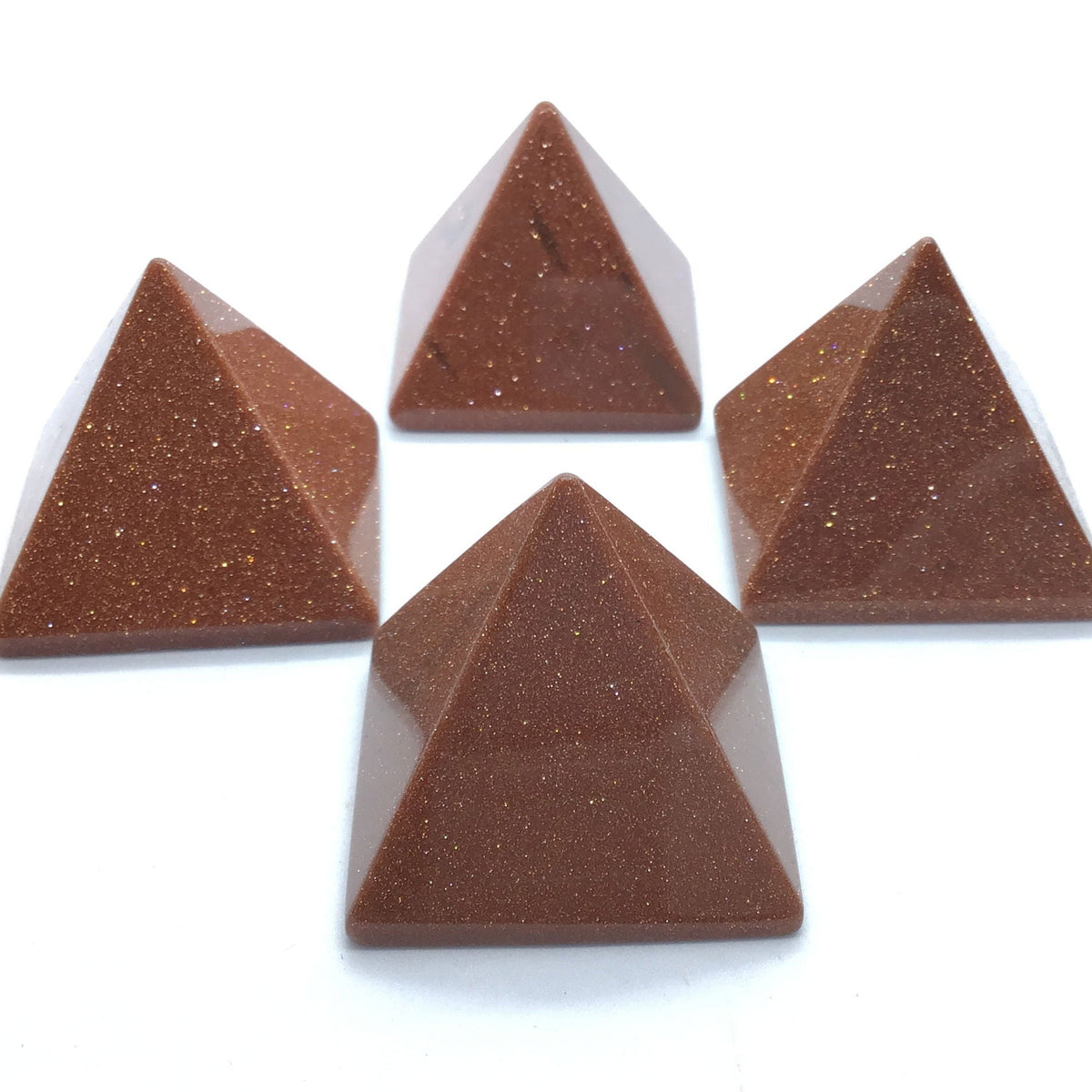 Four sparkling red goldstone pyramids with coppery flecks on white background