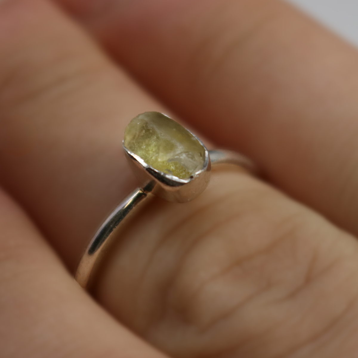 Close-up of a rough freeform Egyptian tektite ring worn on a finger, silver bezel and thin band