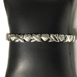 Narrow silver-tone magnetic bracelet with alternating hearts and crossing X links on a display cushion