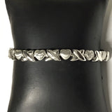 Narrow silver-tone magnetic bracelet with alternating hearts and crossing X links on a display cushion