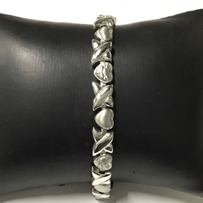 Narrow silver-tone magnetic bracelet with alternating hearts and crossing X links on a display cushion