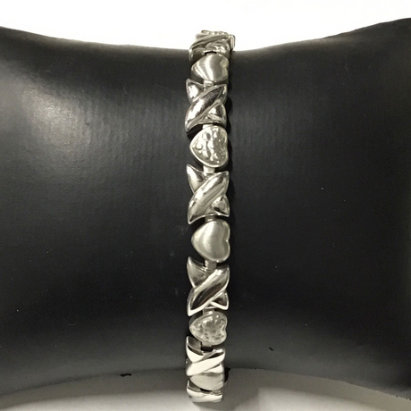 Narrow silver-tone magnetic bracelet with alternating hearts and crossing X links on a display cushion