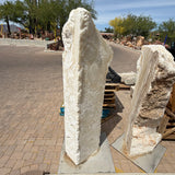 White fossil onyx pillar fountain head-on in a paver drive, creamy banded stone beside a second pillar