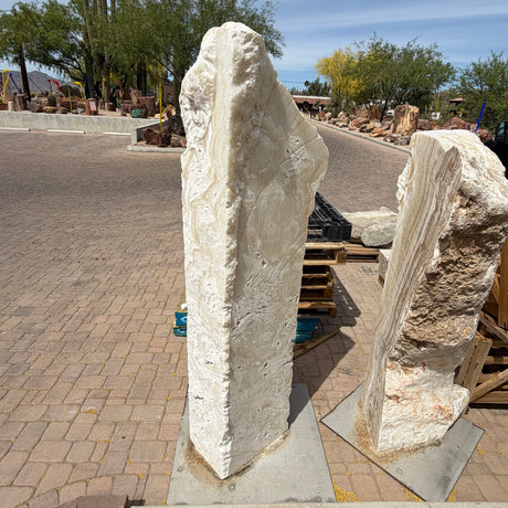 White fossil onyx pillar fountain head-on in a paver drive, creamy banded stone beside a second pillar