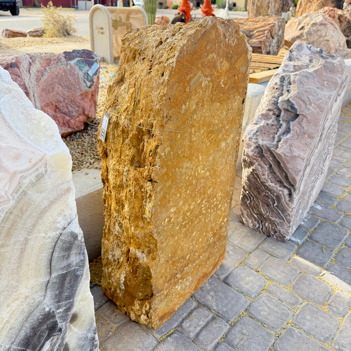 Gold travertine onyx fountain slab seen from the side beside onyx boulders in the gallery stone yard