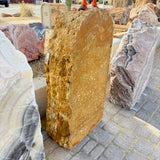 Gold travertine onyx fountain slab seen from the side beside onyx boulders in the gallery stone yard