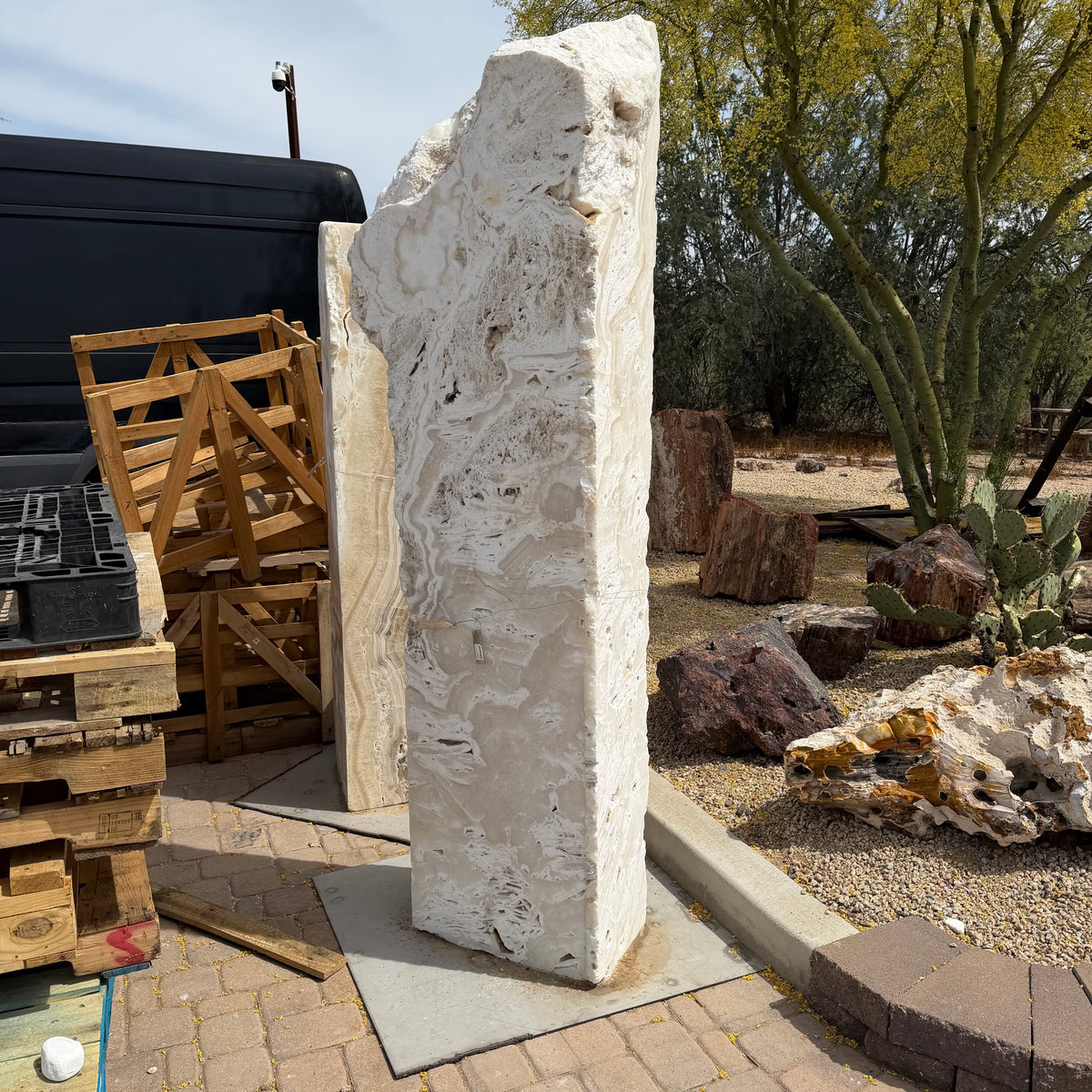 Tall white fossil onyx pillar fountain with nub top and cut sides, standing in a desert stone yard