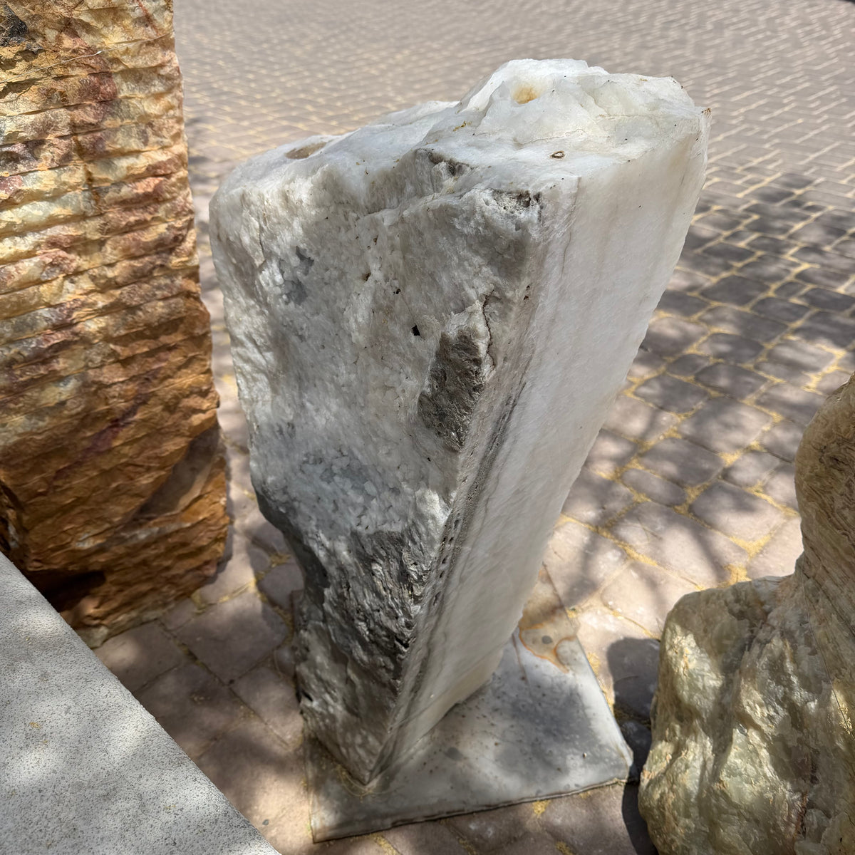 Back of the Ice White Onyx Fountain, gray mineral veining across the wedge-shaped slab on a paver walkway