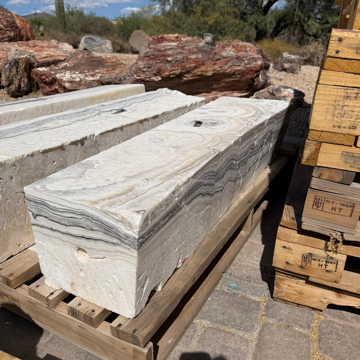 Zebra fossil onyx pillar fountains on pallets in a desert stone yard beside petrified wood boulders