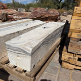 Zebra fossil onyx pillar fountains on pallets in a desert stone yard beside petrified wood boulders
